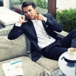 stock image of a man sitting on a couch talking on a cell phone pulling at his collar with a paper next to him