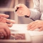 two sets of hands at meeting holding a pen and a iPad