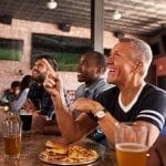 Male Friends At Counter In Sports Bar Watching Game